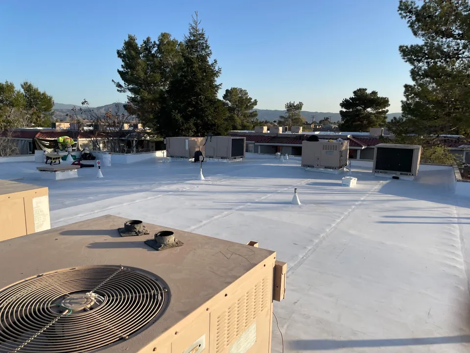 New white flat roof with rooftop AC units and vents, trees and hills behind