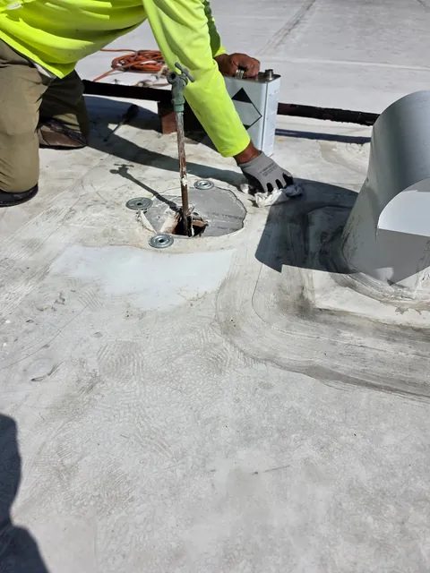 Roofer cleaning around a pipe penetration on a white flat roof