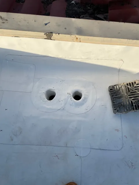 Close-up of two round drain openings flashed into a new white roof membrane, with the drain grate set beside them